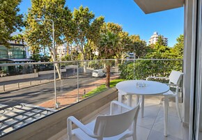 A balcony with a table and chairs, overlooking a street with trees and buildings.