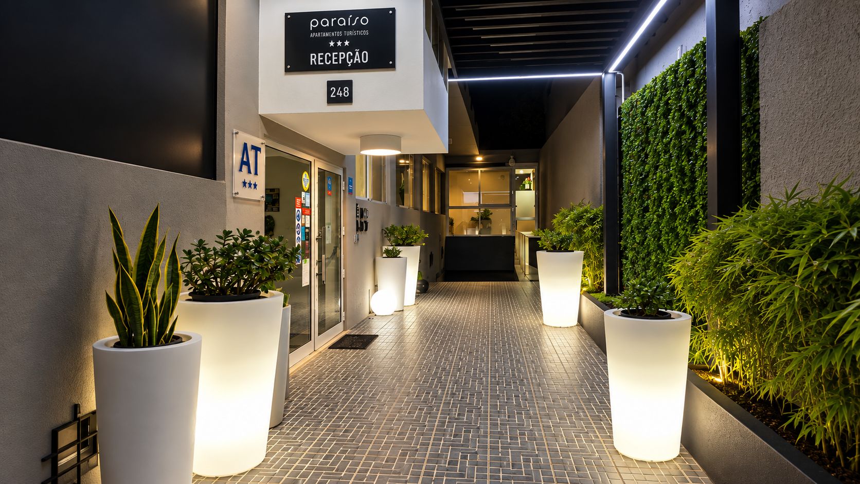 Un pasillo de hotel con recepción, plantas en macetas y un letrero que indica la zona de recepción.