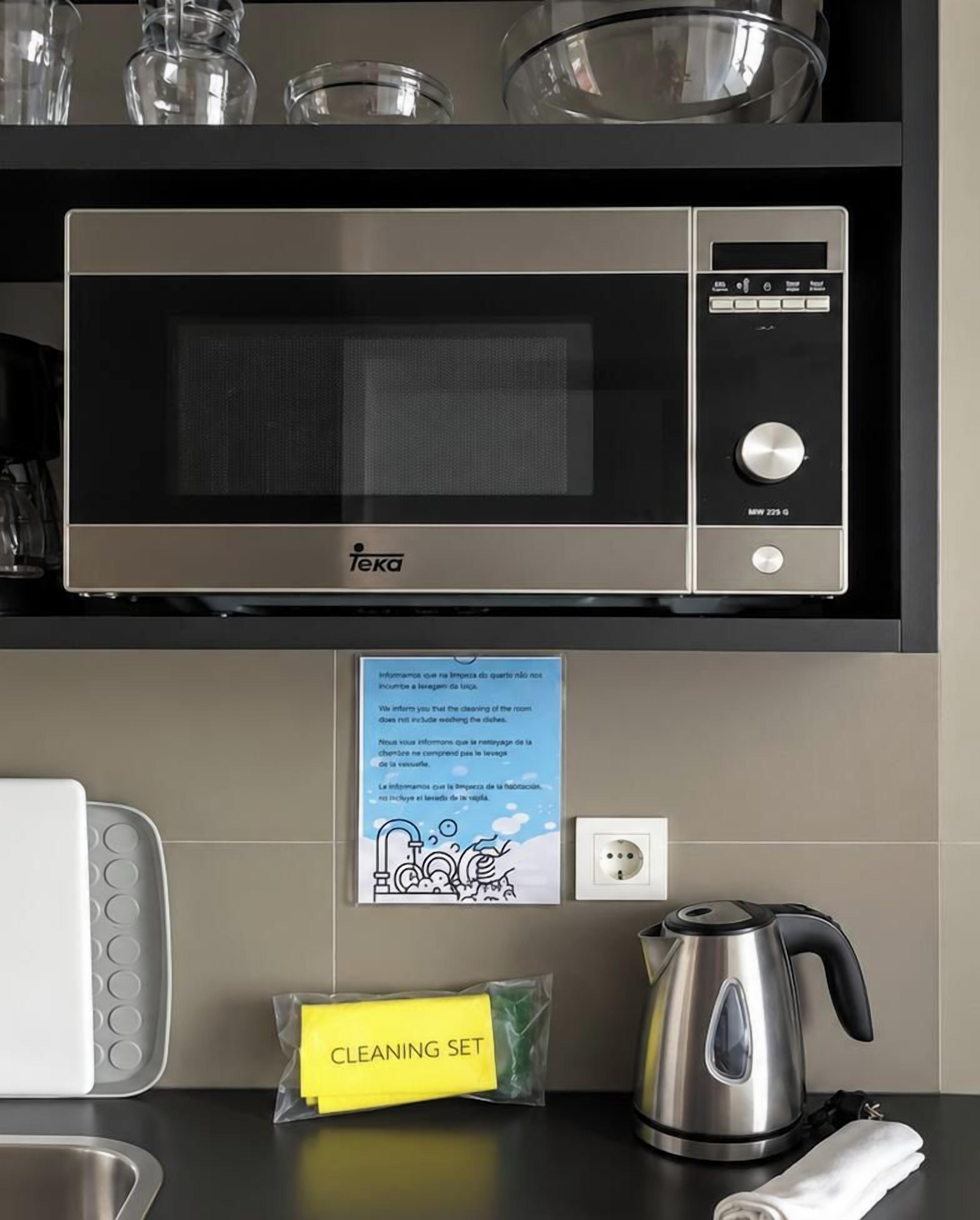 A kitchen with a microwave, a kettle, and a cleaning set.