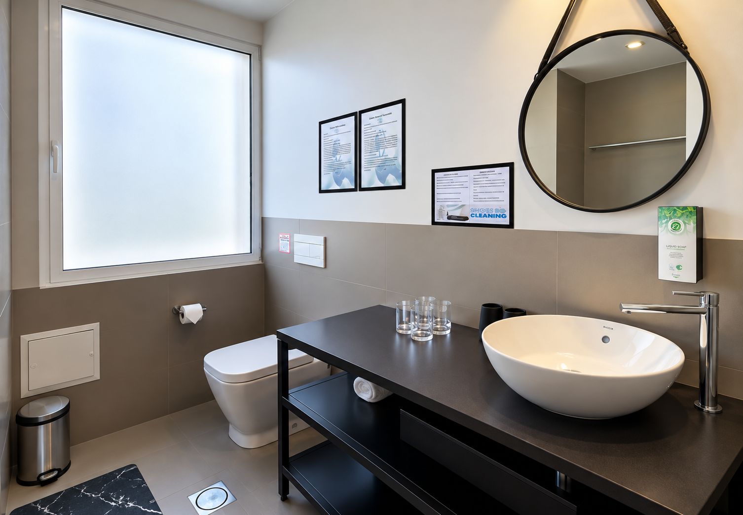 Un baño moderno con un ventanal grande, un lavabo blanco, un espejo y carteles informativos en la pared.