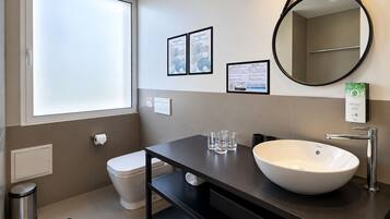 Un baño moderno con un ventanal grande, un lavabo blanco, un espejo y carteles informativos en la pared.