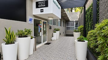 Zona de recepción de hotel con un diseño moderno, que incluye un mostrador de recepción, plantas en macetas y un letrero que indica la ubicación de la recepción.