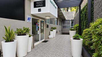 Zona de recepción de hotel con un diseño moderno, que incluye un mostrador de recepción, plantas en macetas y un letrero que indica la ubicación de la recepción.