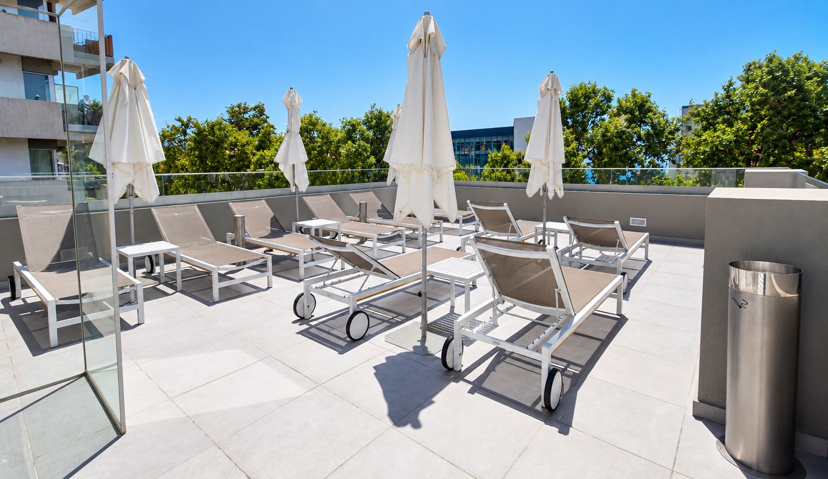 A rooftop lounge area with sun loungers, umbrellas, and a trash can.