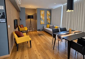 Ein modernes Wohnzimmer mit einer Couch, gelben Sesseln, einem Esstisch und einem Fernseher.