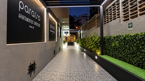 Una entrada de edificio moderno con señalización iluminada para 'Paraiso Apartamentos Turísticos' y un camino que lleva a la entrada.