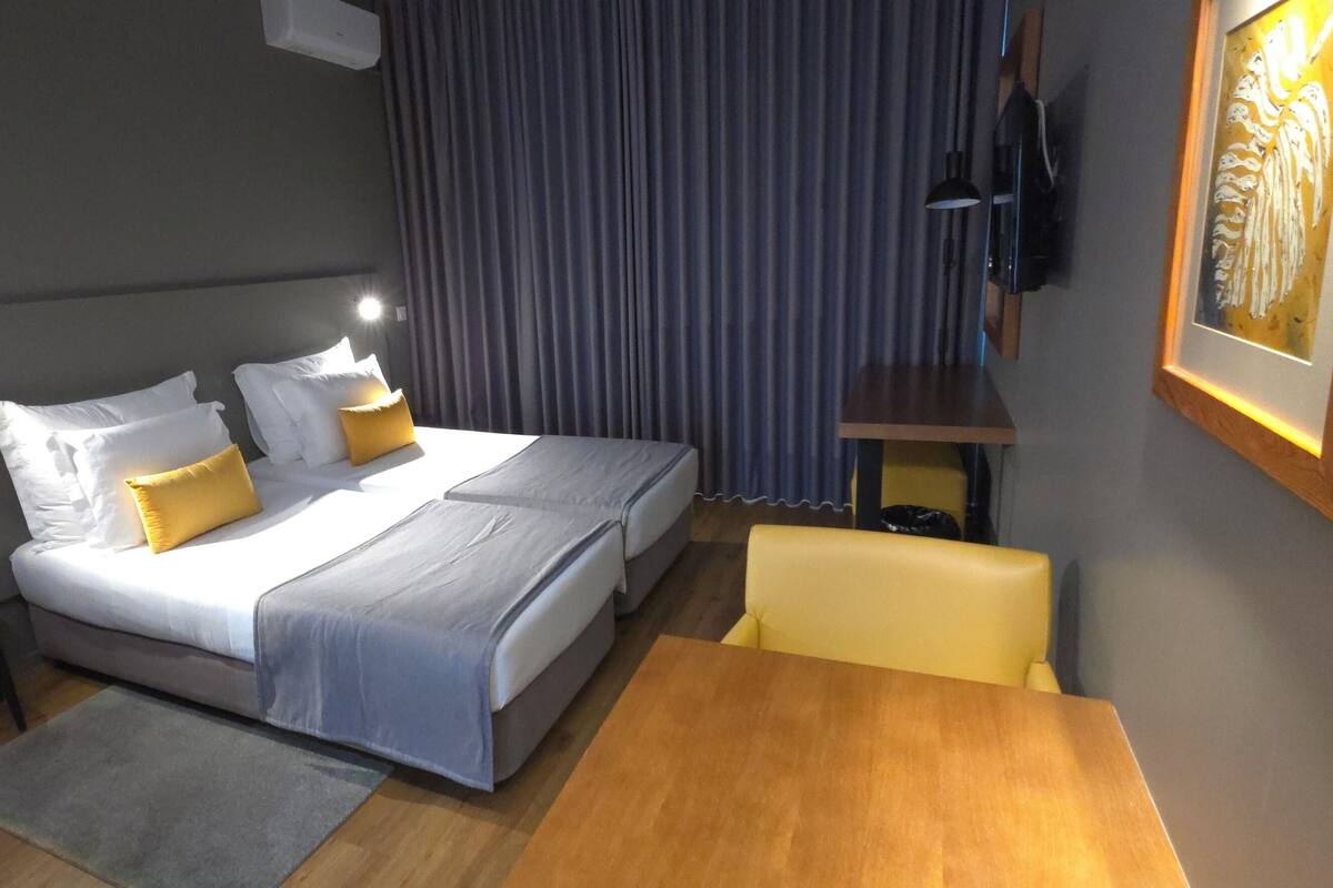 A hotel room with a bed, bedside table, chair, and a painting on the wall.