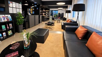 A modern hotel lobby with a reception desk, seating area, and a view of the city.