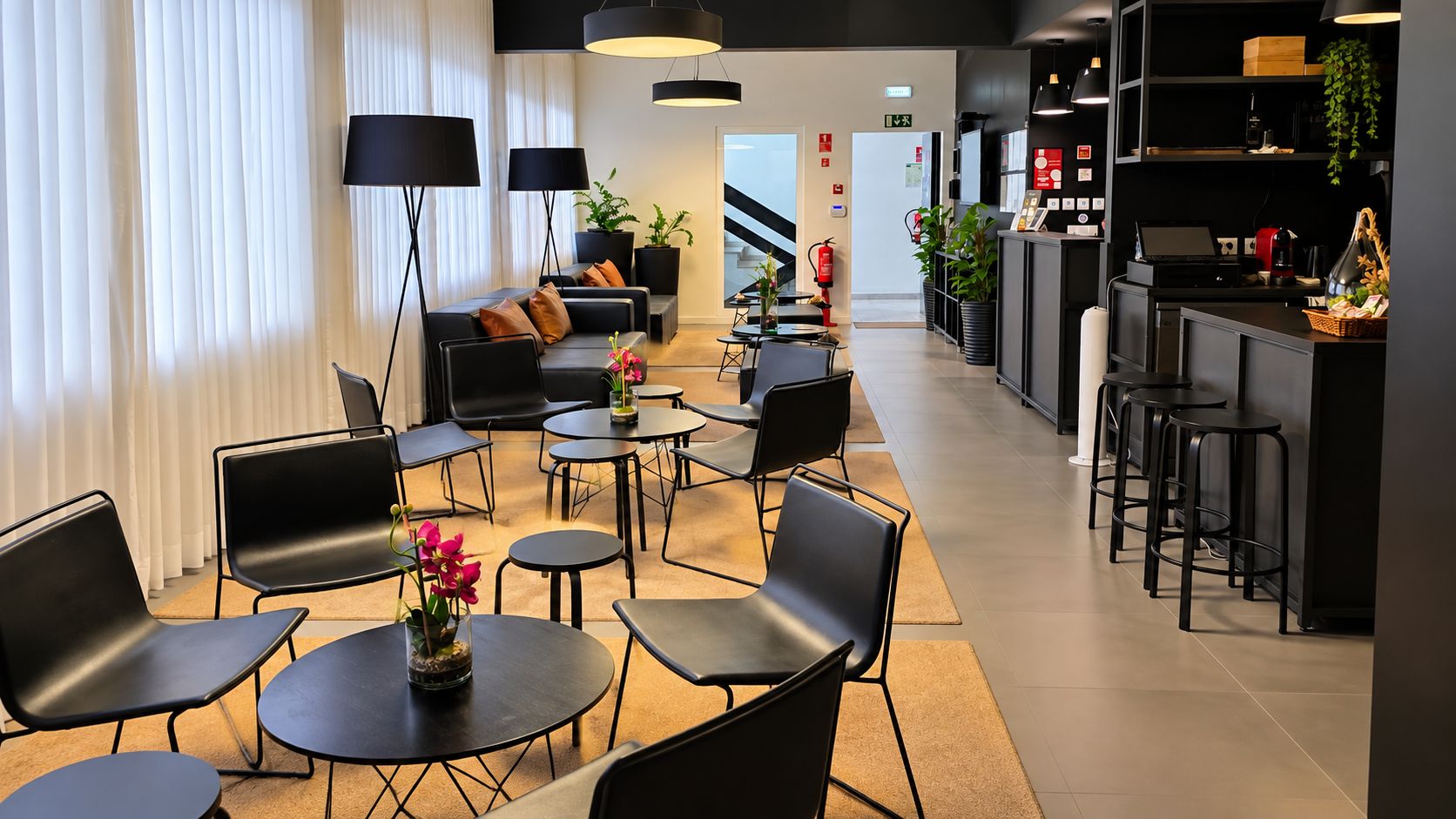 Un moderno vestíbulo de hotel con áreas de descanso, una recepción y una escalera que conduce a otras plantas.