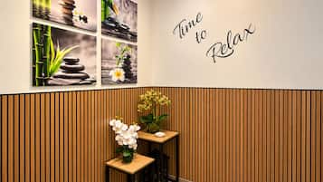 Un espace d’accueil avec une enseigne fixée au mur sur laquelle on peut lire : « Il est temps de se détendre ». On y trouve quatre tableaux encadrés représentant des scènes de nature paisibles, ainsi qu’une petite table en bois sur laquelle est posé un vase rempli de fleurs blanches.