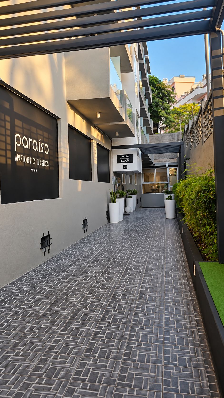 Un edificio moderno con una zona de recepción, plantas en macetas y un camino empedrado.