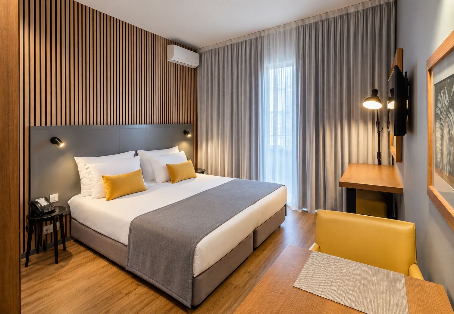 Ein modernes Hotelzimmer mit einem großen Bett, einem Nachttisch, einem Schreibtisch und einem Stuhl.