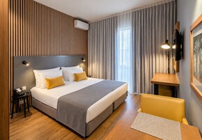 A modern hotel room with a large bed, a bedside table, a desk, and a chair.