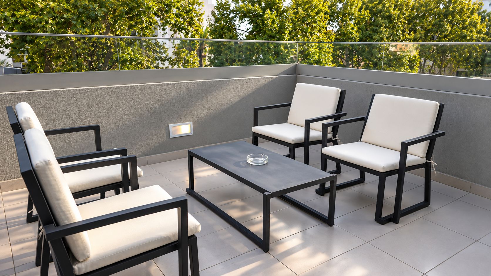 A rooftop terrace with a table and four chairs, a glass of water on the table, and a wall-mounted light fixture.