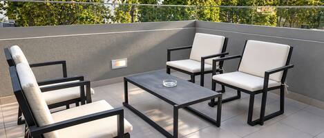 A rooftop terrace with a table and four chairs, a glass of water on the table, and a wall-mounted light fixture.