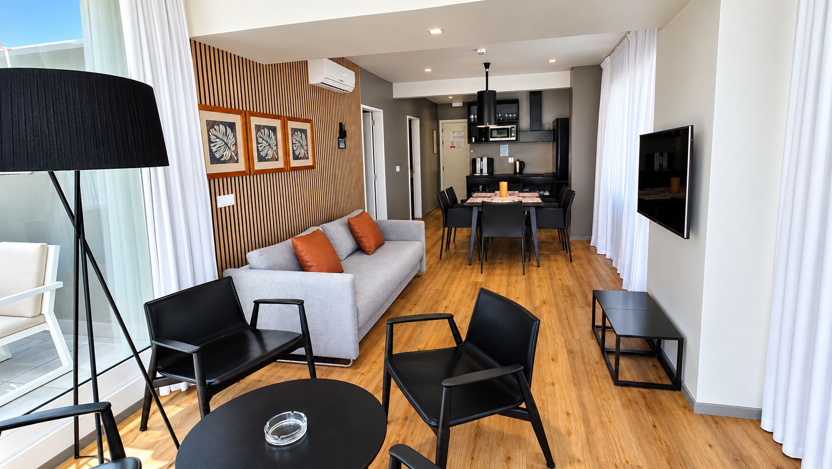 Una habitación de hotel moderna con sofá, sillas, una mesa de comedor y televisor.