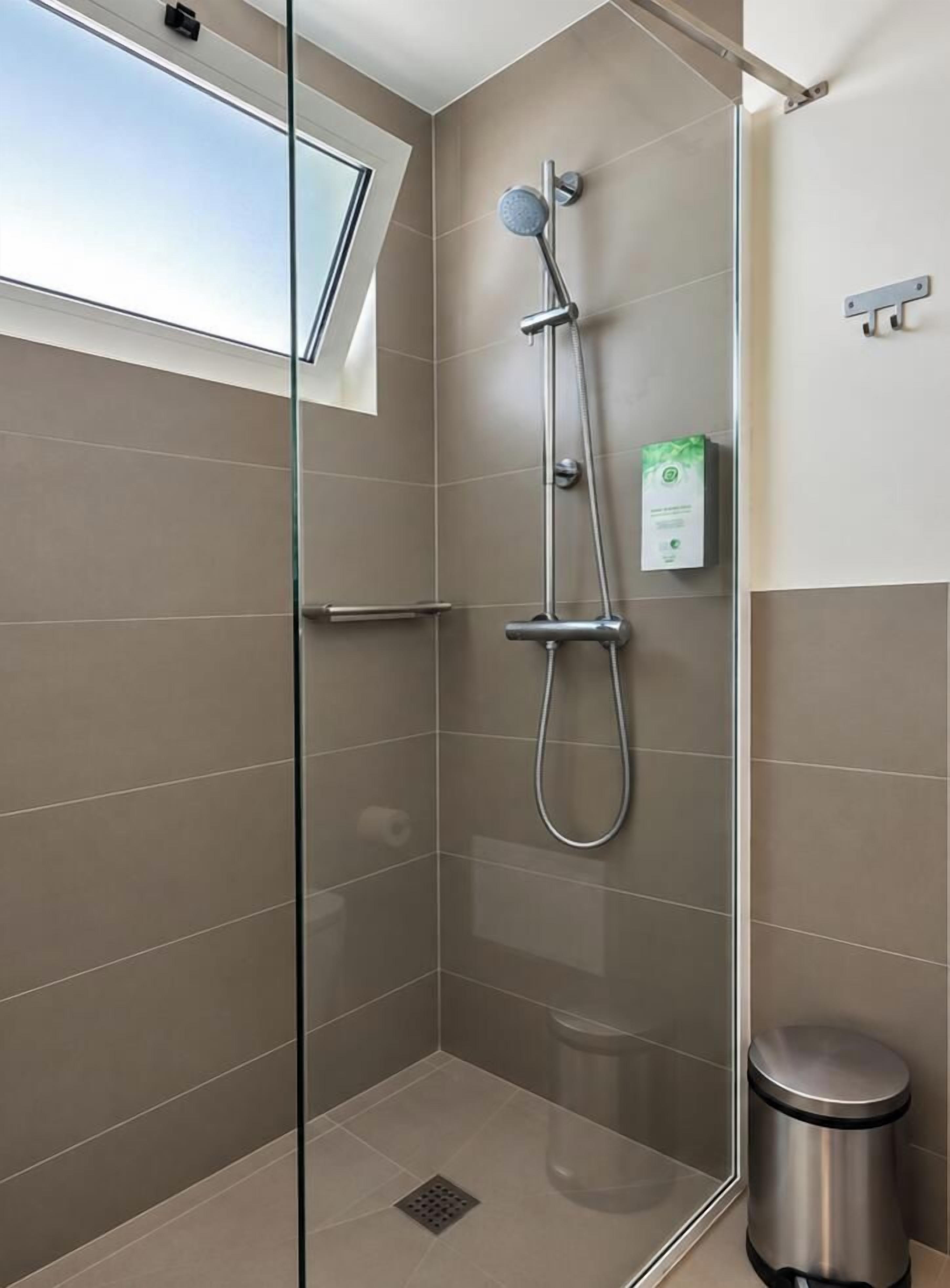 Ducha moderna con puerta de vidrio, cabezal de ducha de mano y panel de control en la pared.