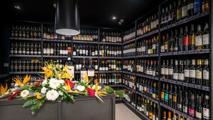 A wine cellar with shelves of wine bottles and a floral centerpiece. - Paraíso - Touristic Apartments (Funchal)