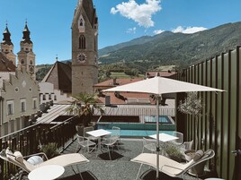 Terraza en la azotea con sillones de descanso, piscina y vistas a una iglesia histórica y montañas.