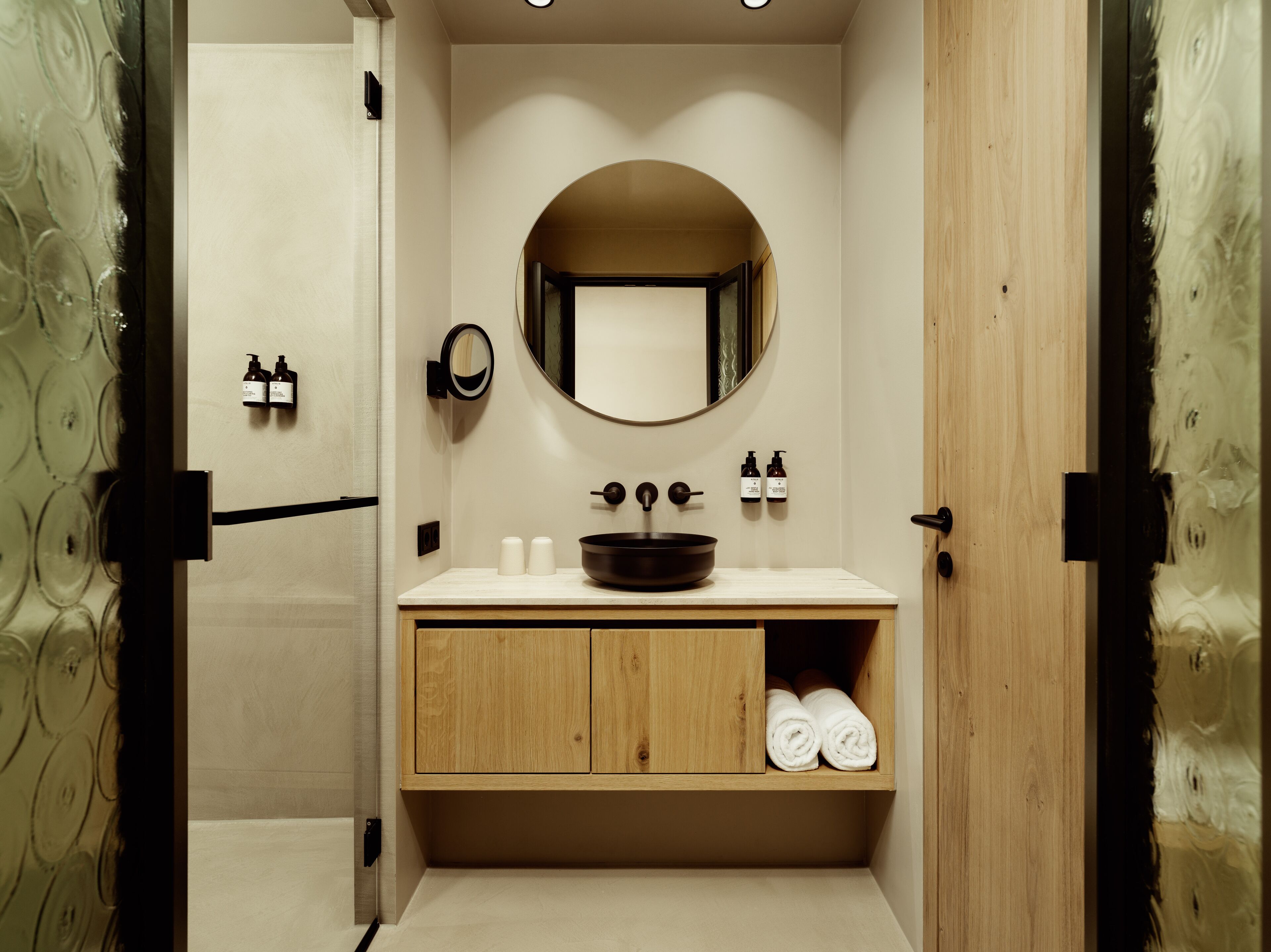 A modern bathroom with a round mirror, wooden vanity, and a built-in towel rack.