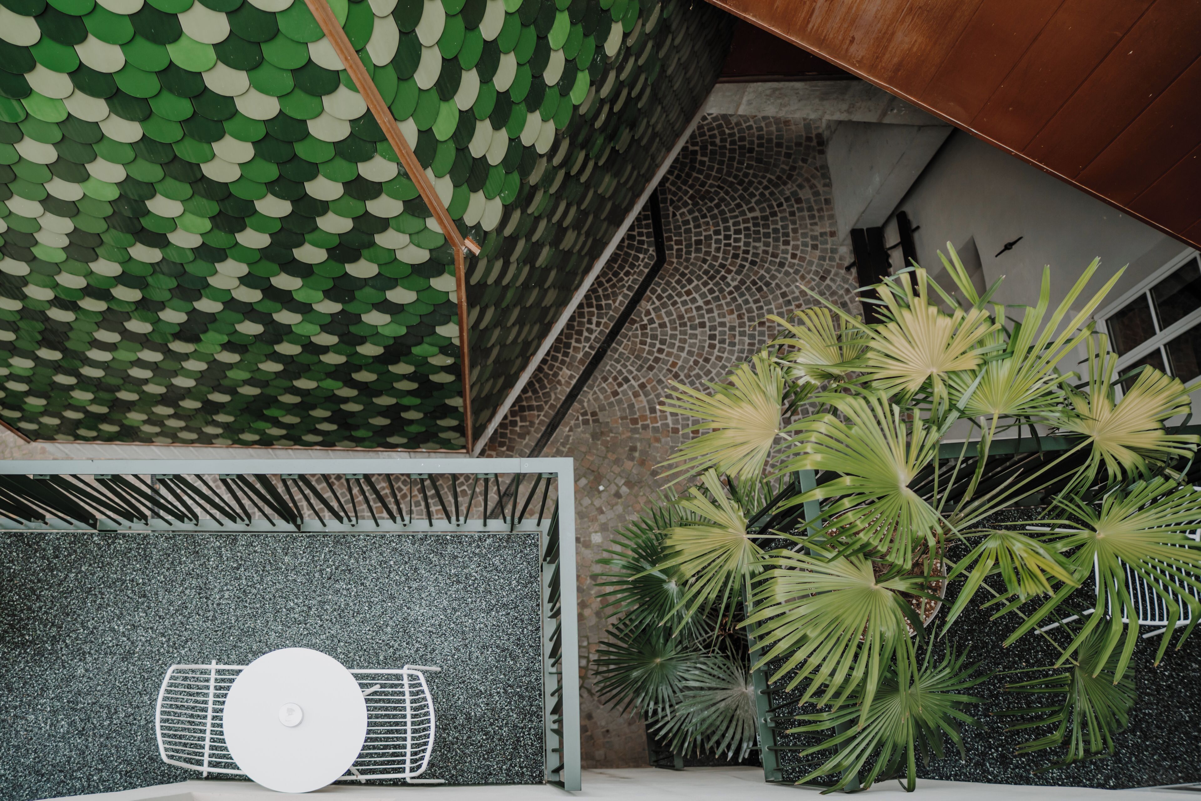 Un interior moderno con techo estampado en hojas verdes, un ventilador blanco y plantas de palma verdes.
