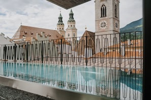 Zona de piscina con una cerca metálica, una torre del reloj y dos torres puntiagudas al fondo.