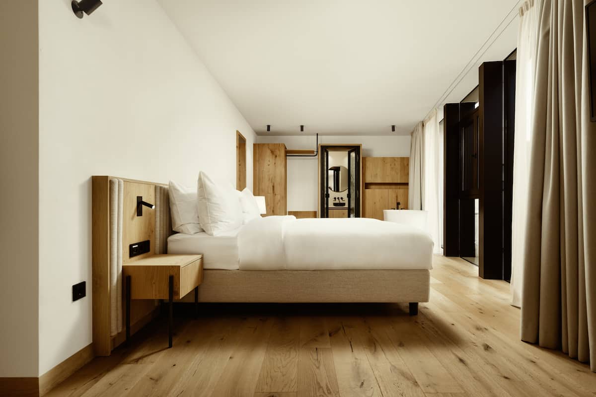 A modern bedroom with a large bed, wooden headboard, bedside tables, and a wardrobe.