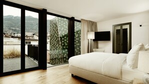 Habitación de hotel con una cama grande, un televisor montado en la pared y un balcón con vistas a las montañas.