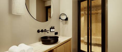 Un baño moderno con un espejo redondo, un lavabo negro y un mueble de tocador de madera.