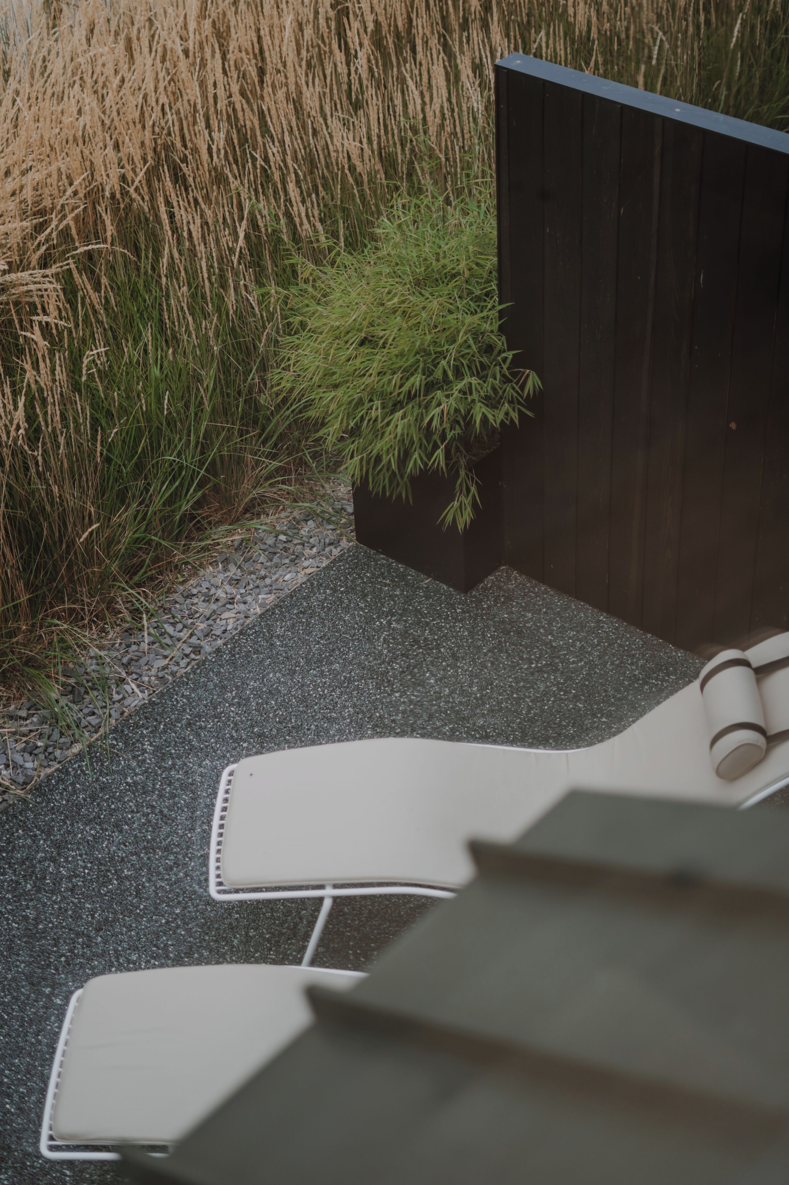 A patio area with a black fence, a small planter with green plants, and a pair of white lounge chairs.