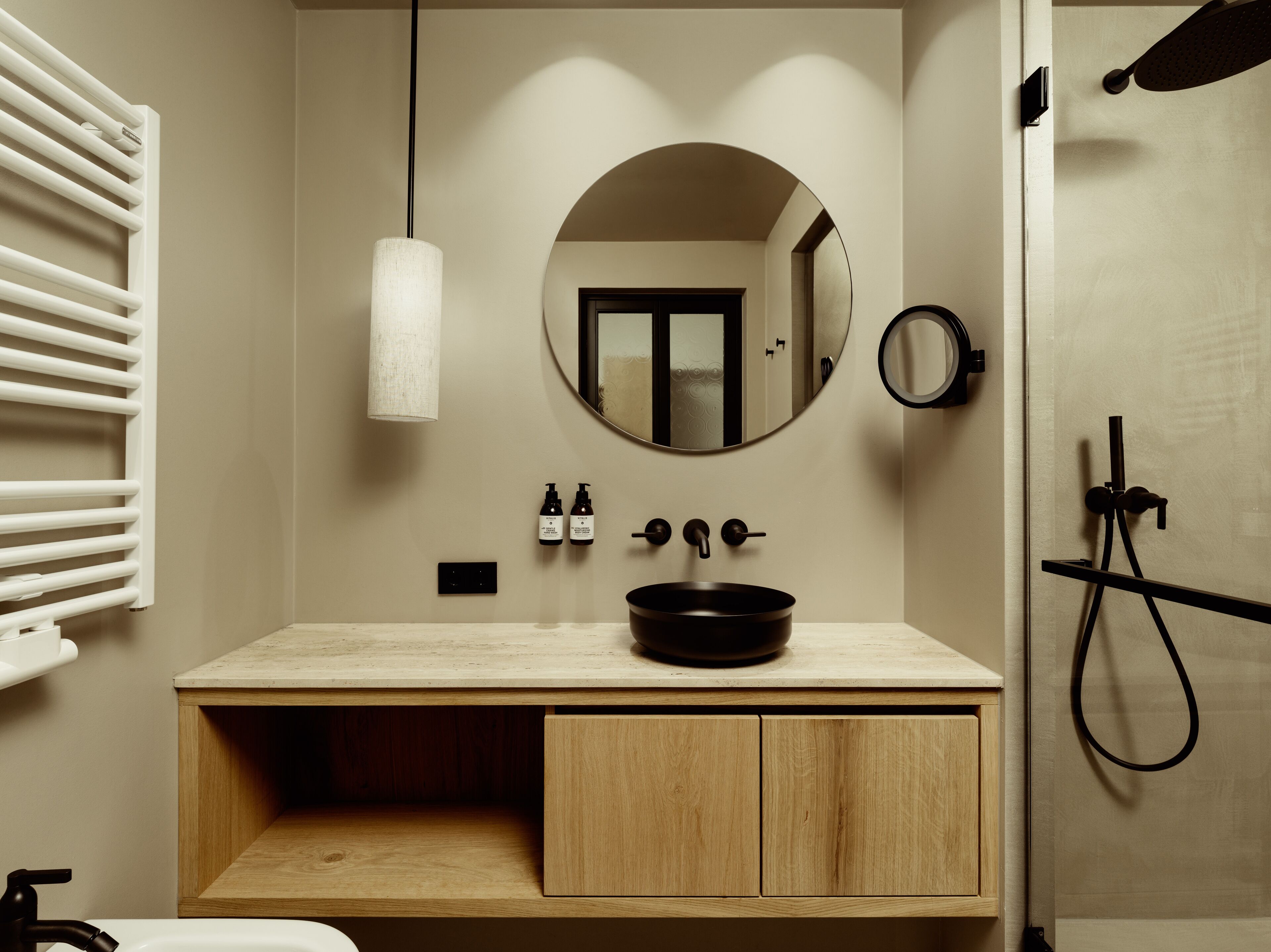 A modern bathroom with a wooden vanity, a round mirror, a black sink, and a towel rack.