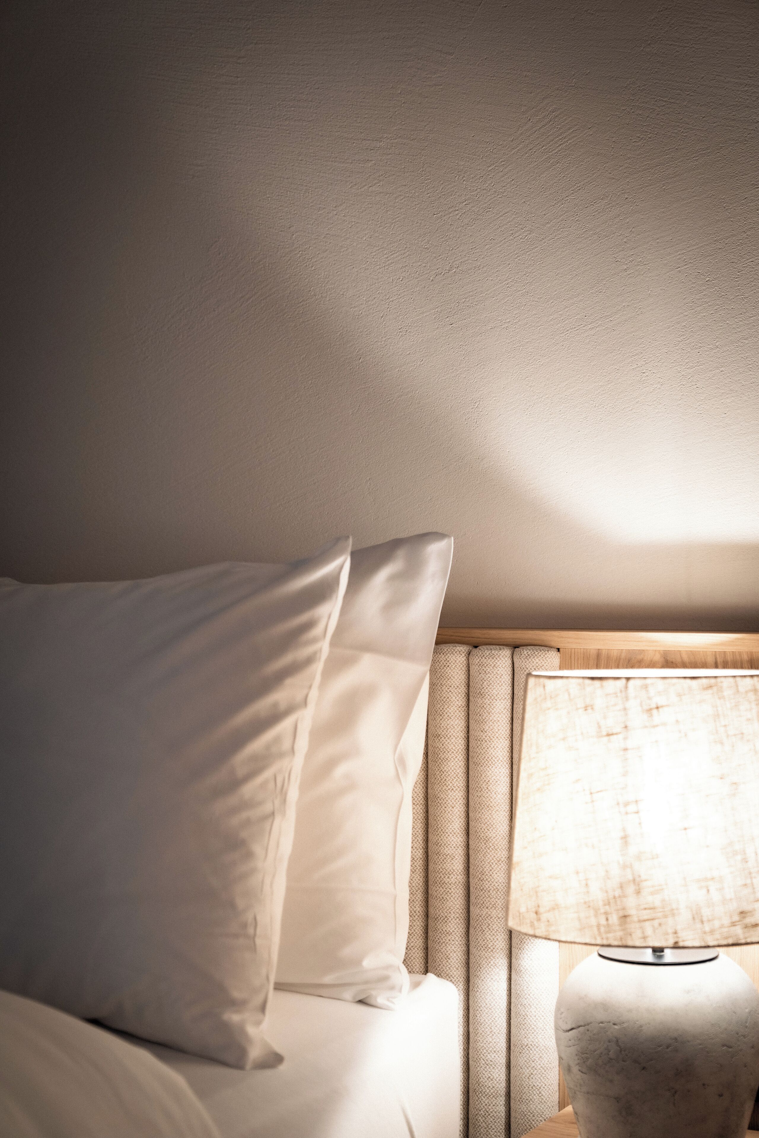 Ein ordentlich bezogenes Bett mit weißen Leinen und einer Lampe auf einem Nachttisch.