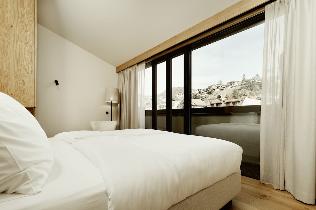 A bedroom with a bed, a chair, a lamp, and a view of a snowy landscape through a window.