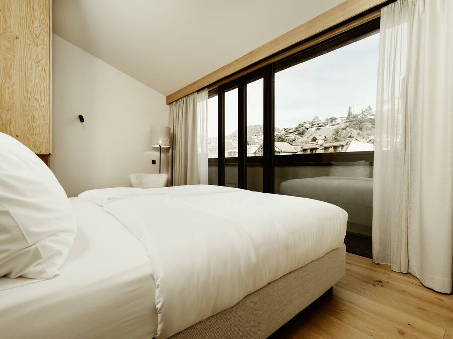 A bedroom with a bed, a chair, a lamp, and a view of a snowy landscape through a window.