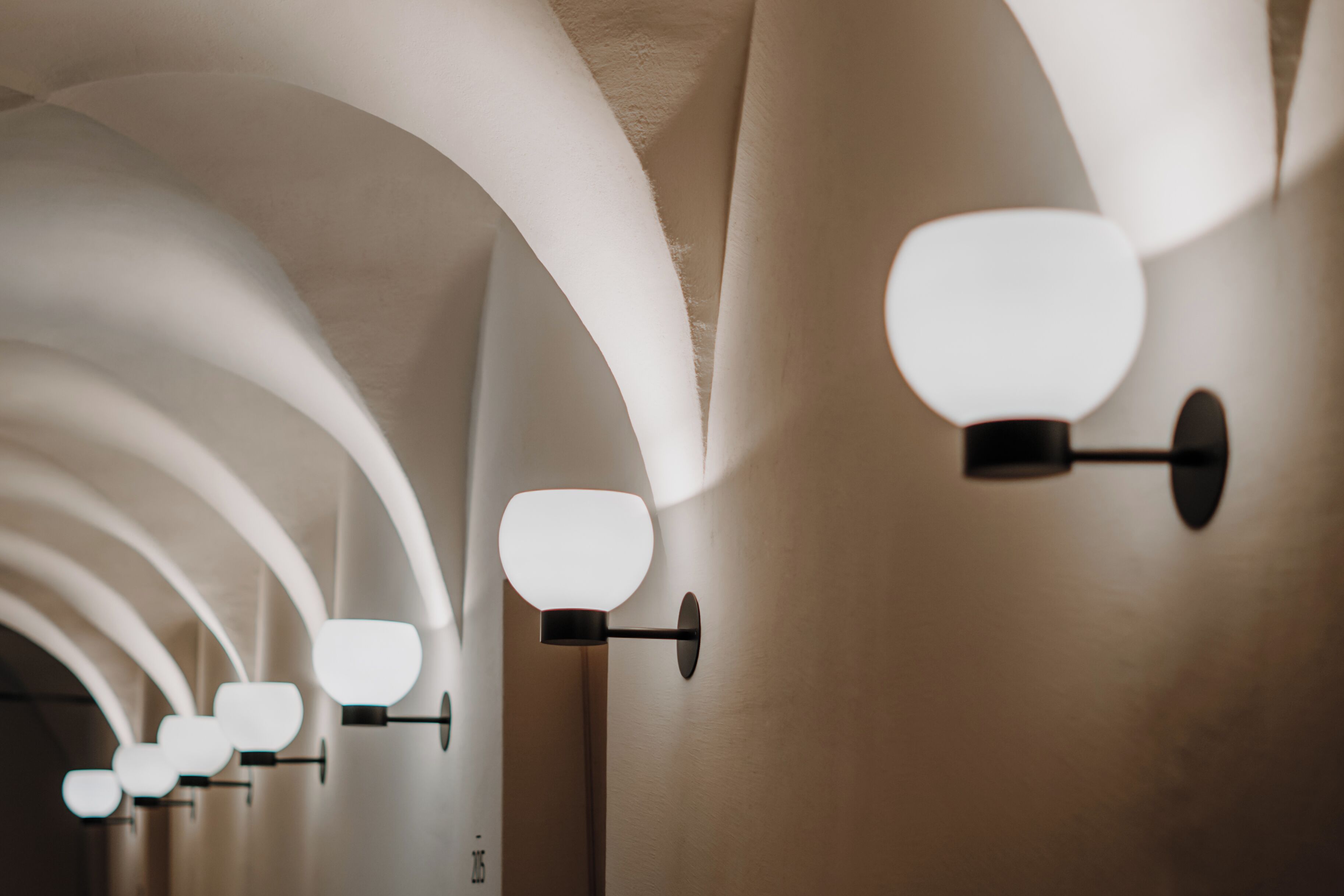 A series of wall-mounted light fixtures with a modern design, arranged in a linear pattern along a curved ceiling.