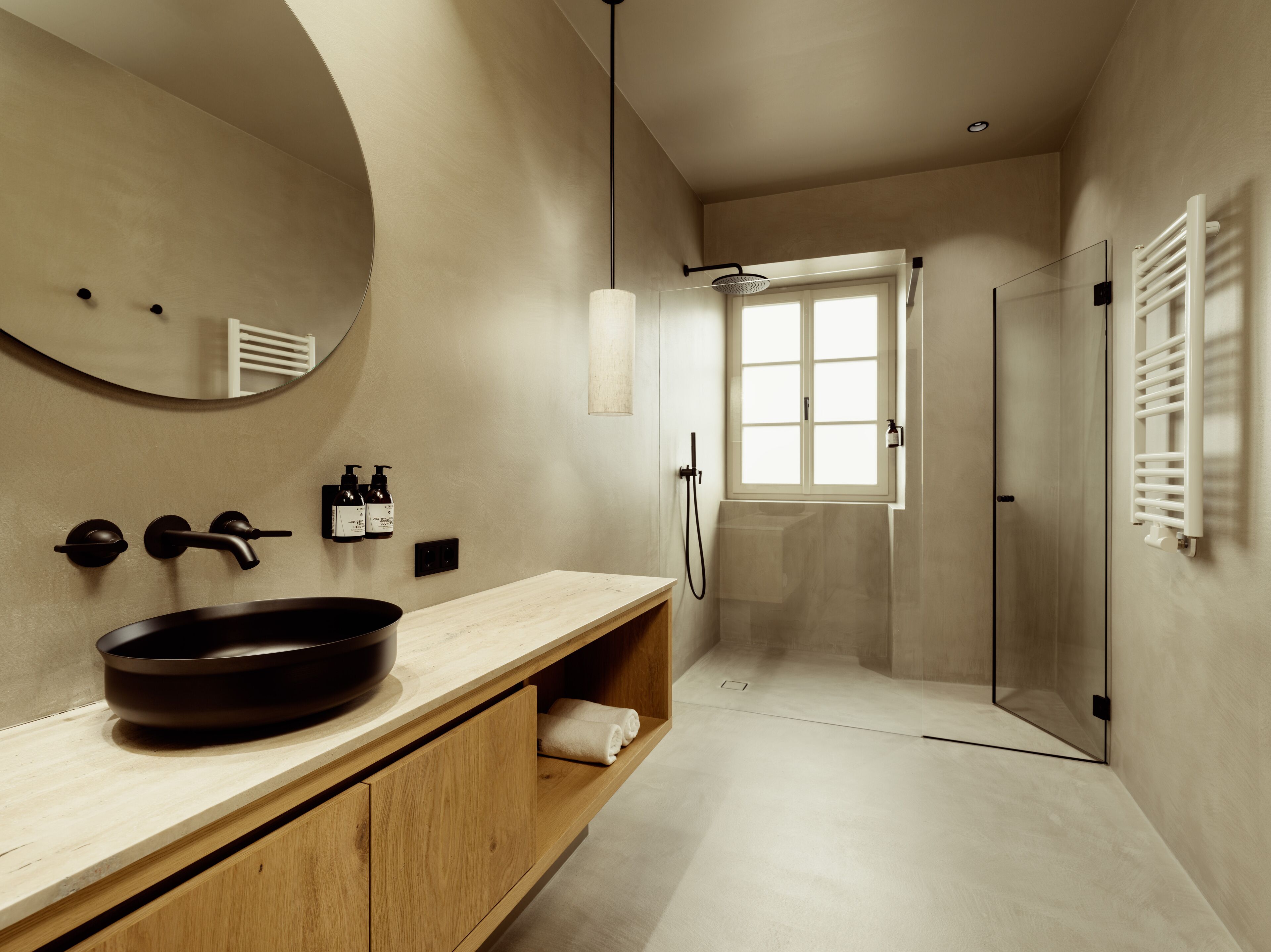 A modern bathroom with a large mirror, a round sink, a shower, and a towel rack.