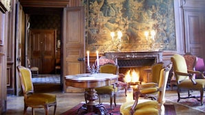 A traditional room with a fireplace, wooden furniture, and a large tapestry. - Château de Ternay (Ternay)