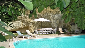 A swimming pool with lounge chairs and an umbrella, surrounded by greenery and a stone wall. - Château de Ternay (Ternay)