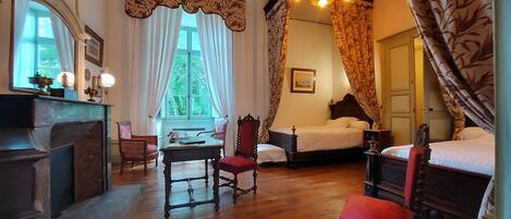 A traditional room with a wooden floor, a desk with a lamp, a chair, a bed with a canopy, and a door.