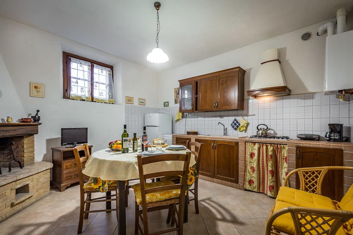 Een keuken met een eettafel, stoelen, een open haard, een fornuis en een raam met gordijnen.