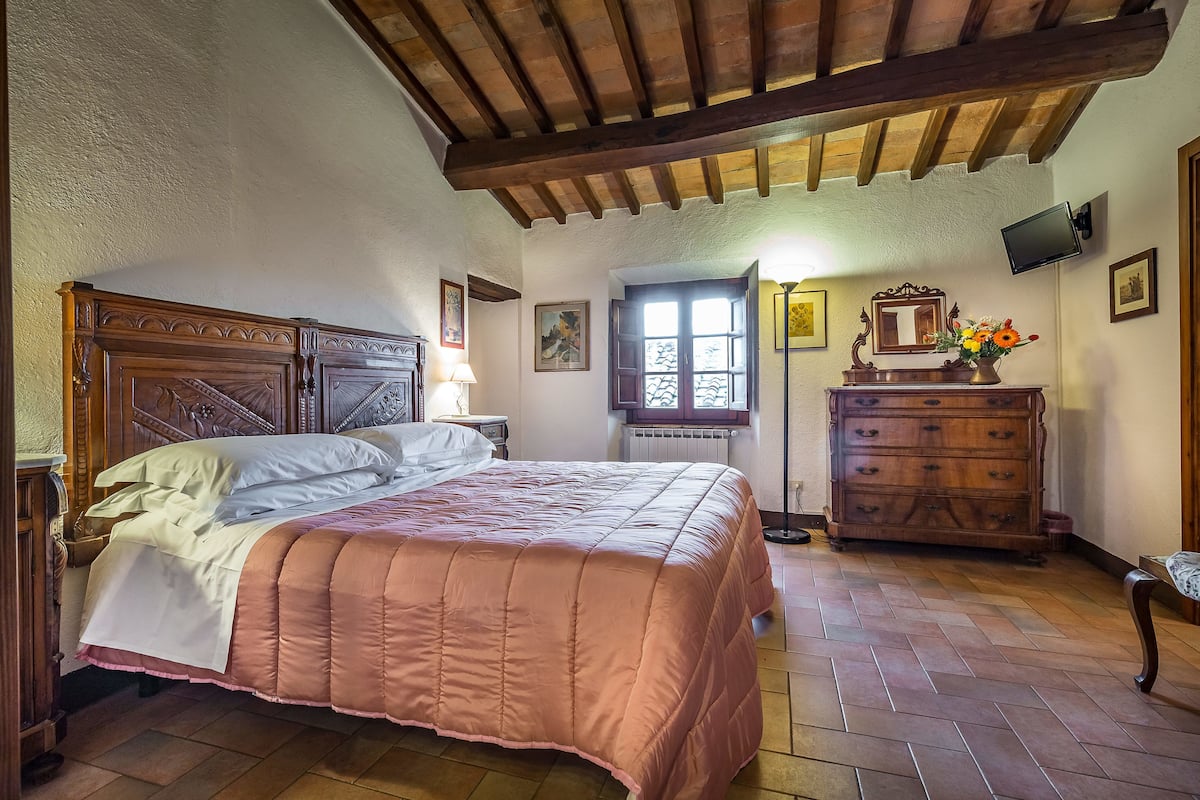 Een slaapkamer met een houten bed, een dressoir en een raam met uitzicht.