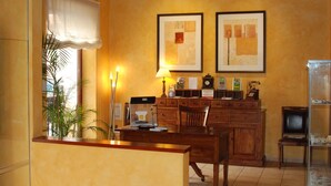 A room with a wooden desk, a lamp, framed artwork on the wall, and a television on a stand. - L'Àgora Hotel (Bocairente)