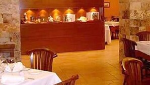 A restaurant with a wooden counter, tables with white tablecloths, and chairs. - L'Àgora Hotel (Bocairente)