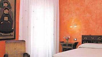 Habitació d'hotel amb un llit, una cadira, un quadre a la paret i una cortina.