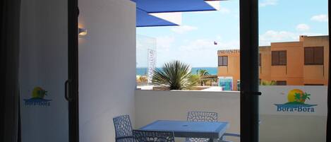 A balcony with a table and chairs, a view of the sea, and a building with a sign reading "Bora-Bora".