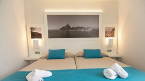 Ein Doppelbett mit zwei Kissen, einer türkisfarbenen Bettdecke und zwei aufgerollten Handtüchern.