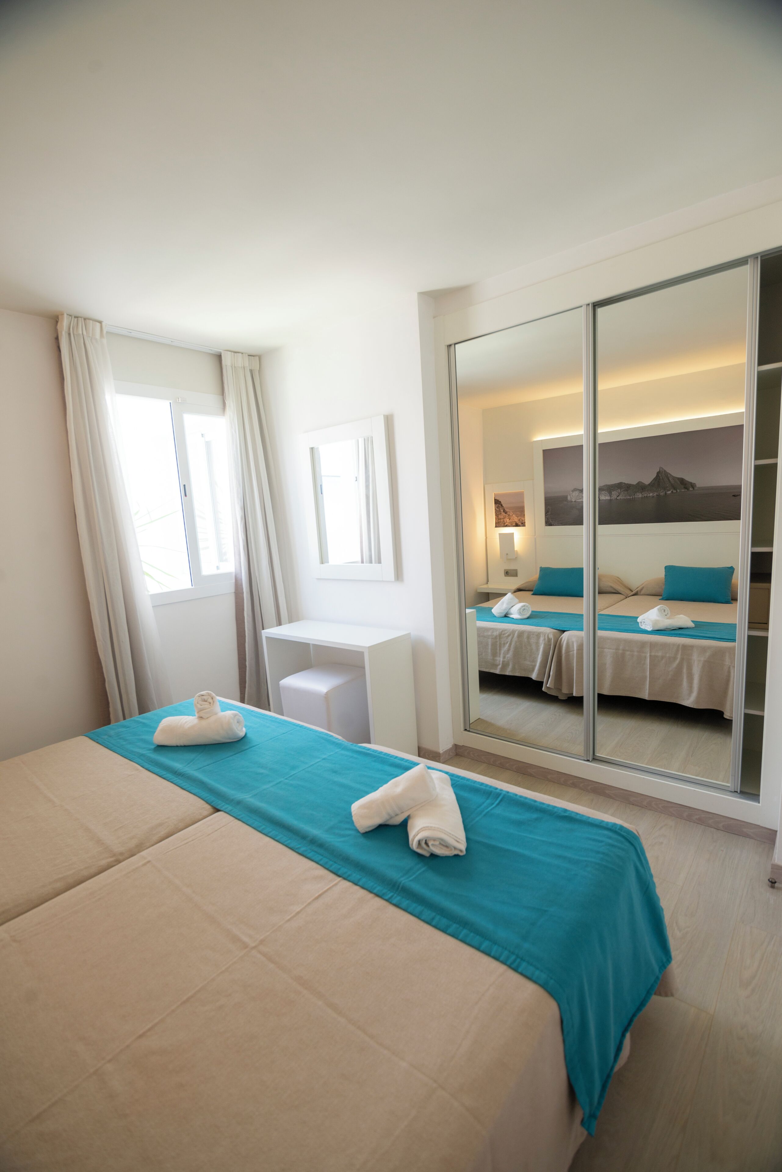 Habitación de hotel con una cama grande, un escritorio, un espejo y una puerta corredera que da a otra habitación.
