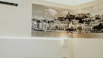 Un dormitorio con una cama, dos almohadas azules, una mesita de noche montada en la pared y un cartel grande con una vista urbana.