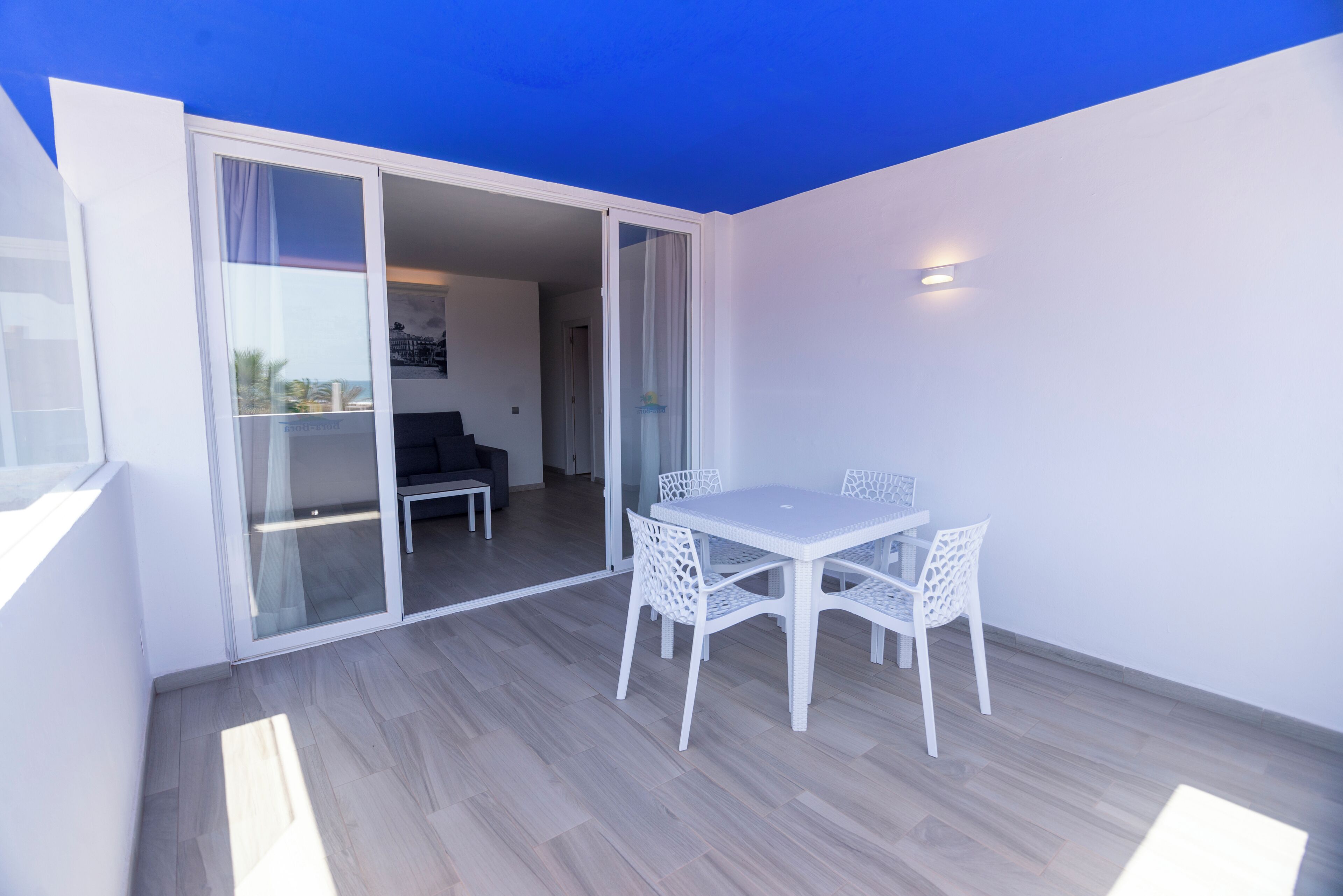 Varanda com mesa e cadeiras, porta de correr de vidro e vista para um quarto interno.