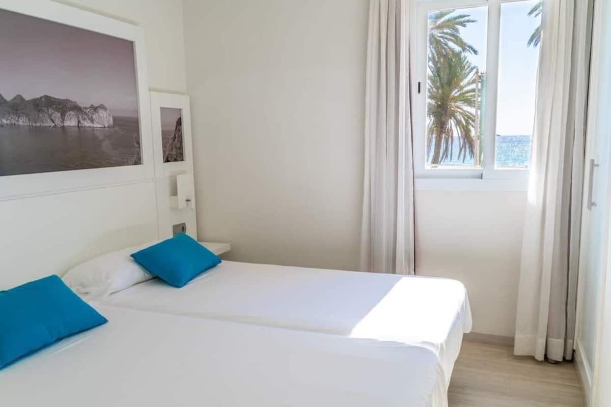 Una habitación de hotel con dos camas, un ventanal con cortinas y un cuadro en la pared.